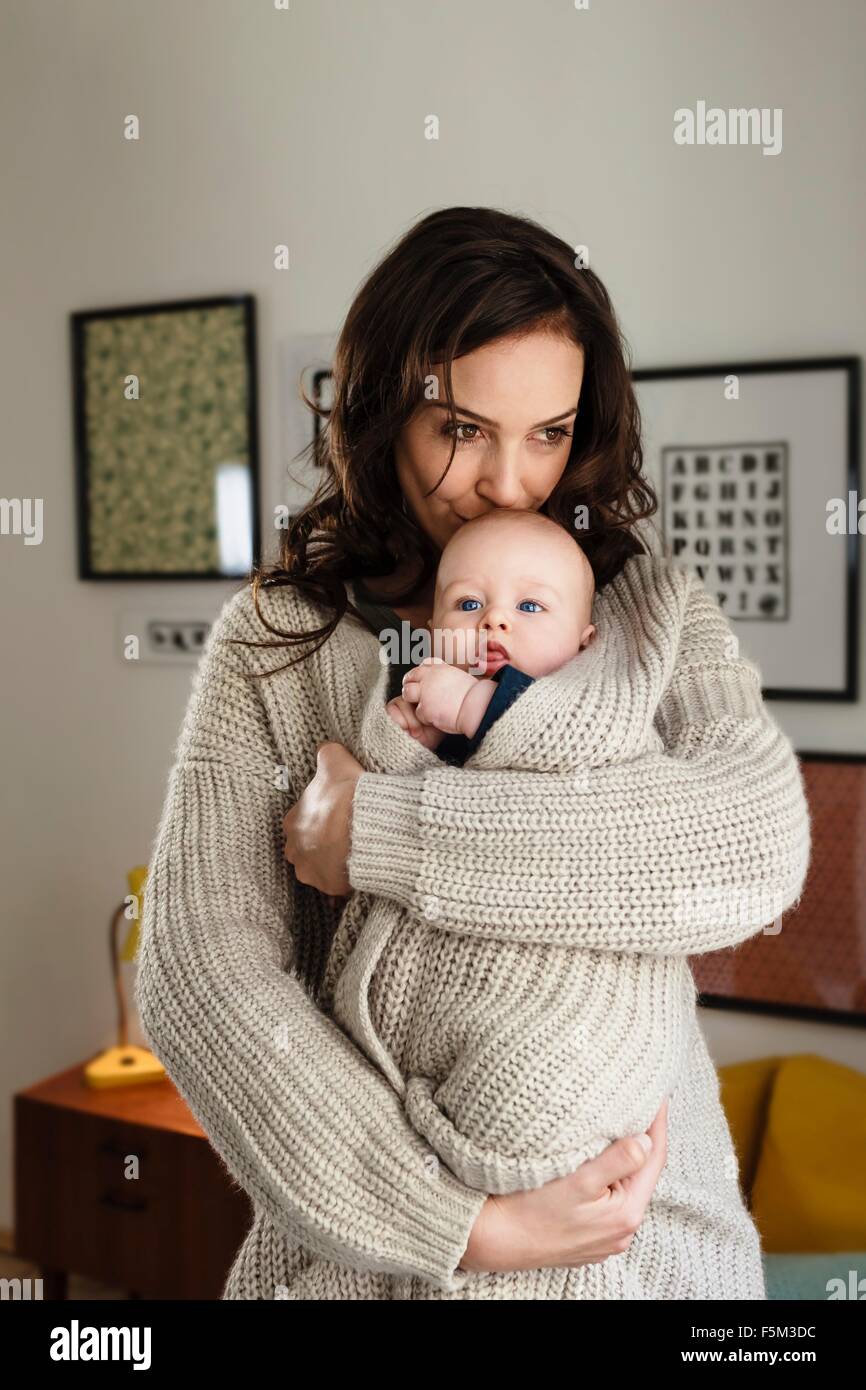 Woman kissing baby son, wrapping him in her cardigan Stock Photo