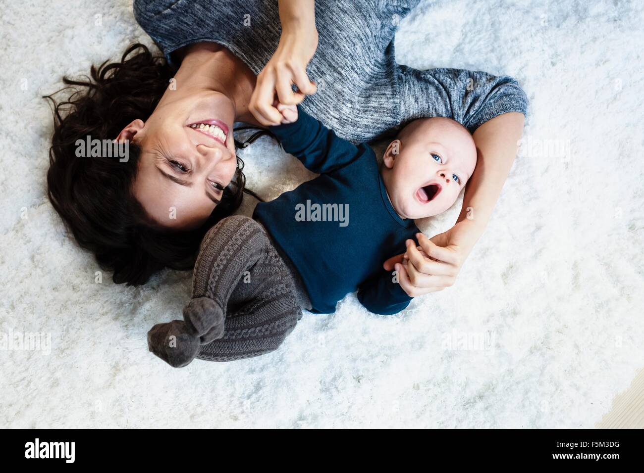 Mother lying on rug with baby son, overhead view Stock Photo