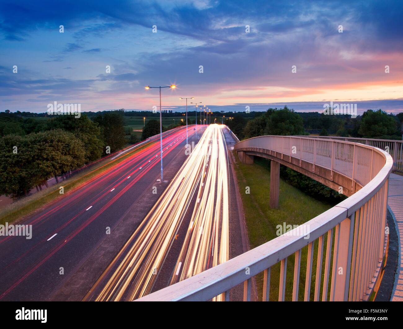 Elevated view of footbridge and highway traffic light trails at dusk Stock Photo