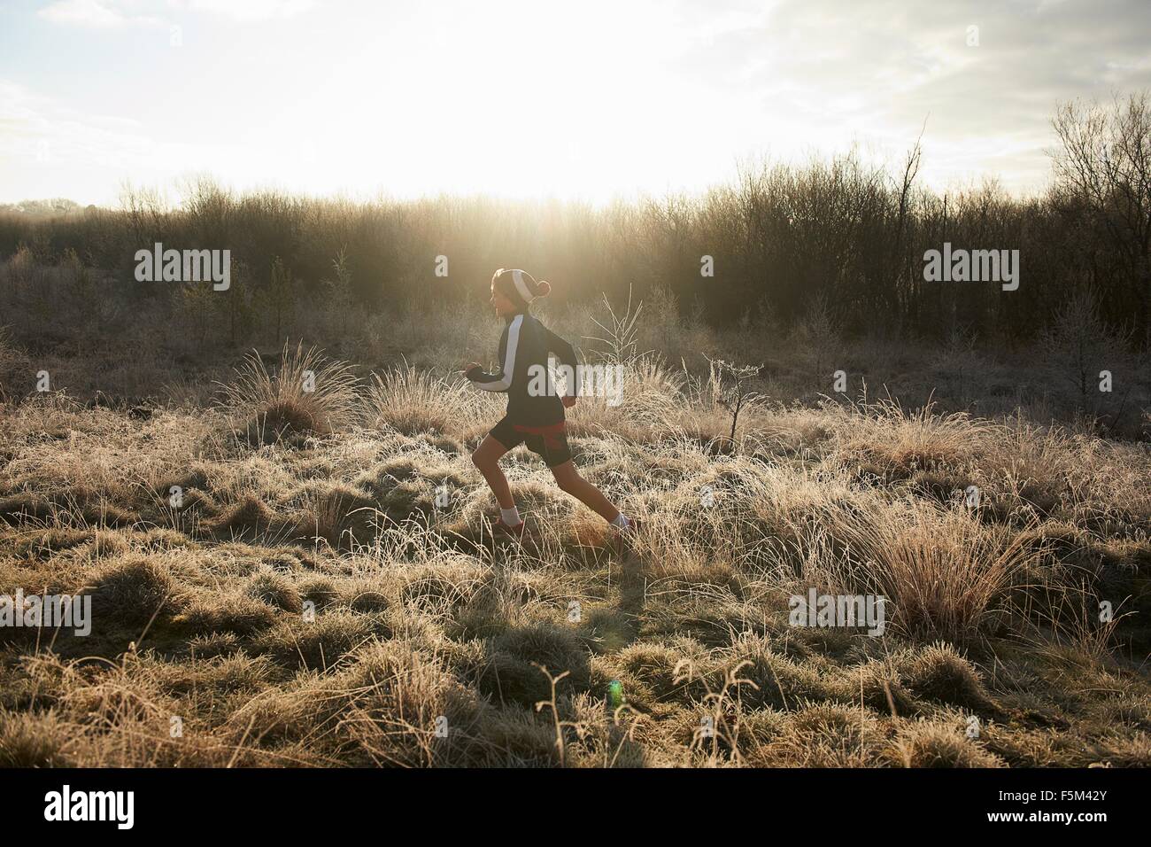 Side view of teenage boy running on frosty grassland Stock Photo