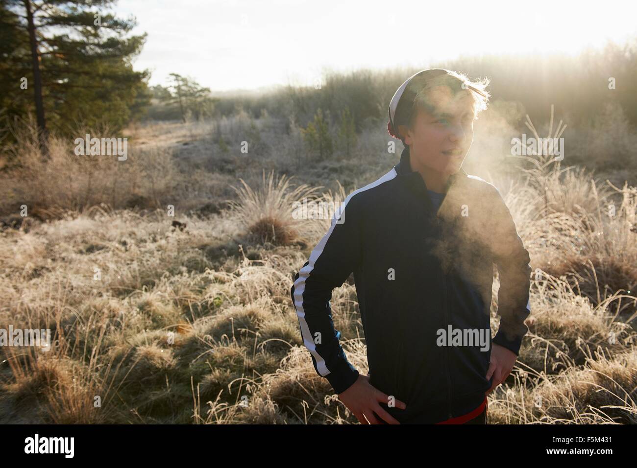 Teenage boy on frosty grassland, visible breath, hands on hips looking away Stock Photo