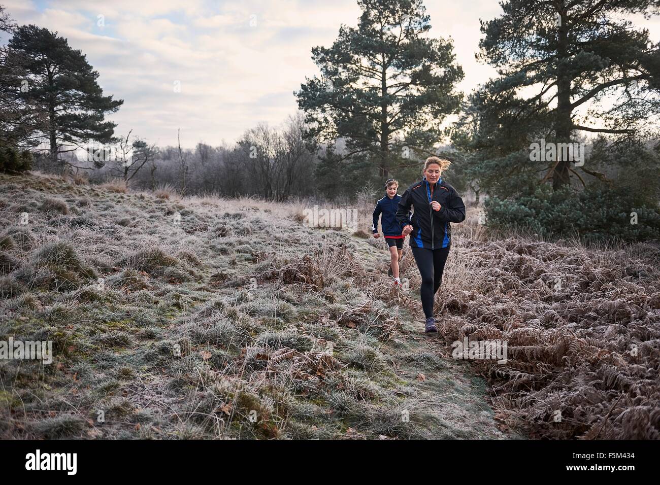Front view of mother and son running on frosty grassland Stock Photo