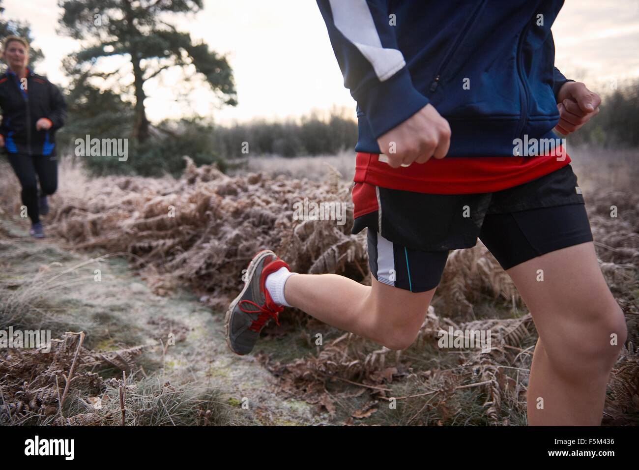 Cropped low angle view of mother and son jogging on frosty grassland Stock Photo