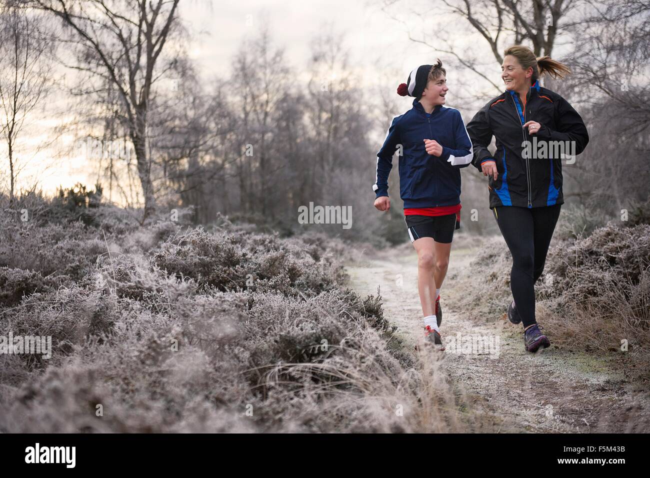 Front view of mother and son running on frosty path face to face smiling Stock Photo
