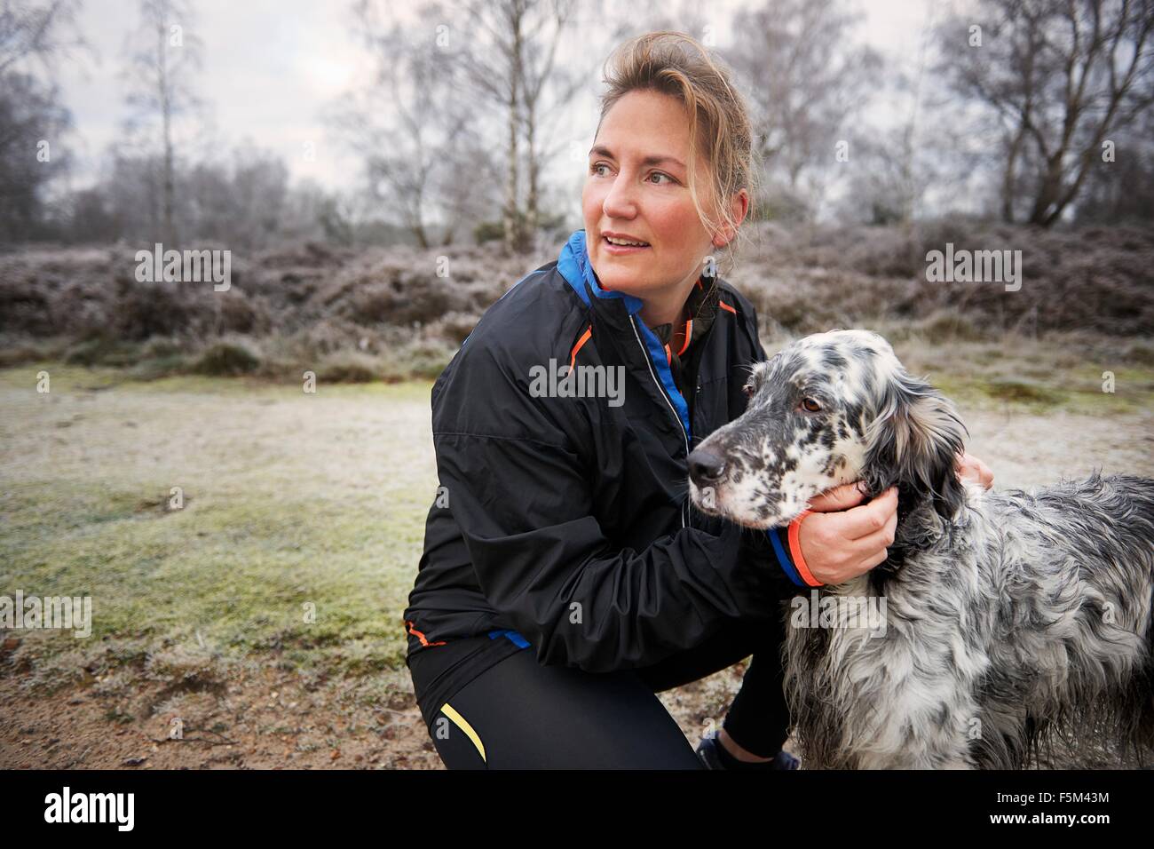 Mature woman crouching down stroking dog looking away Stock Photo