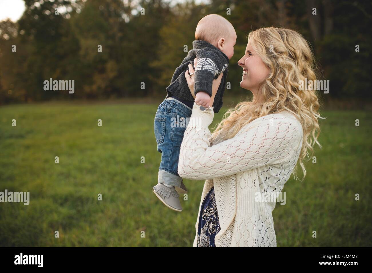 Mid adult woman holding up baby son in field Stock Photo