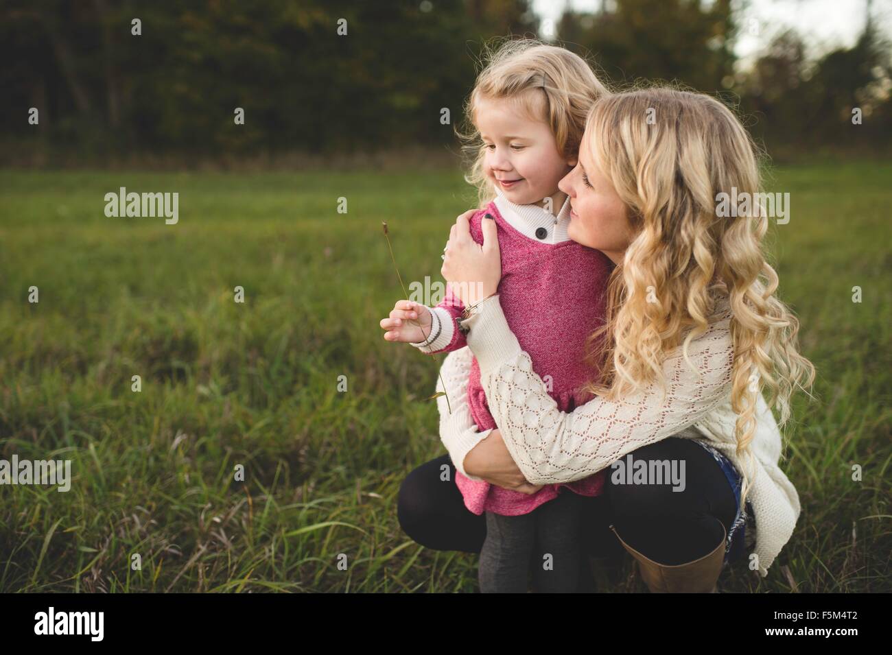 Mid adult woman and daughter holding stem of grass in field Stock Photo