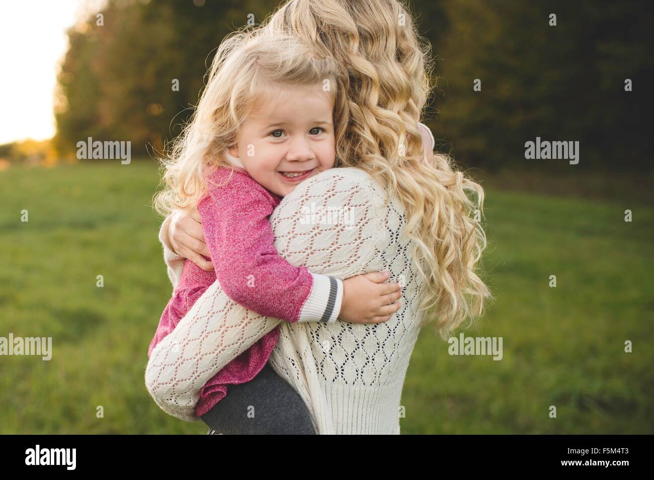 Portrait of mid adult woman hugging daughter in field Stock Photo