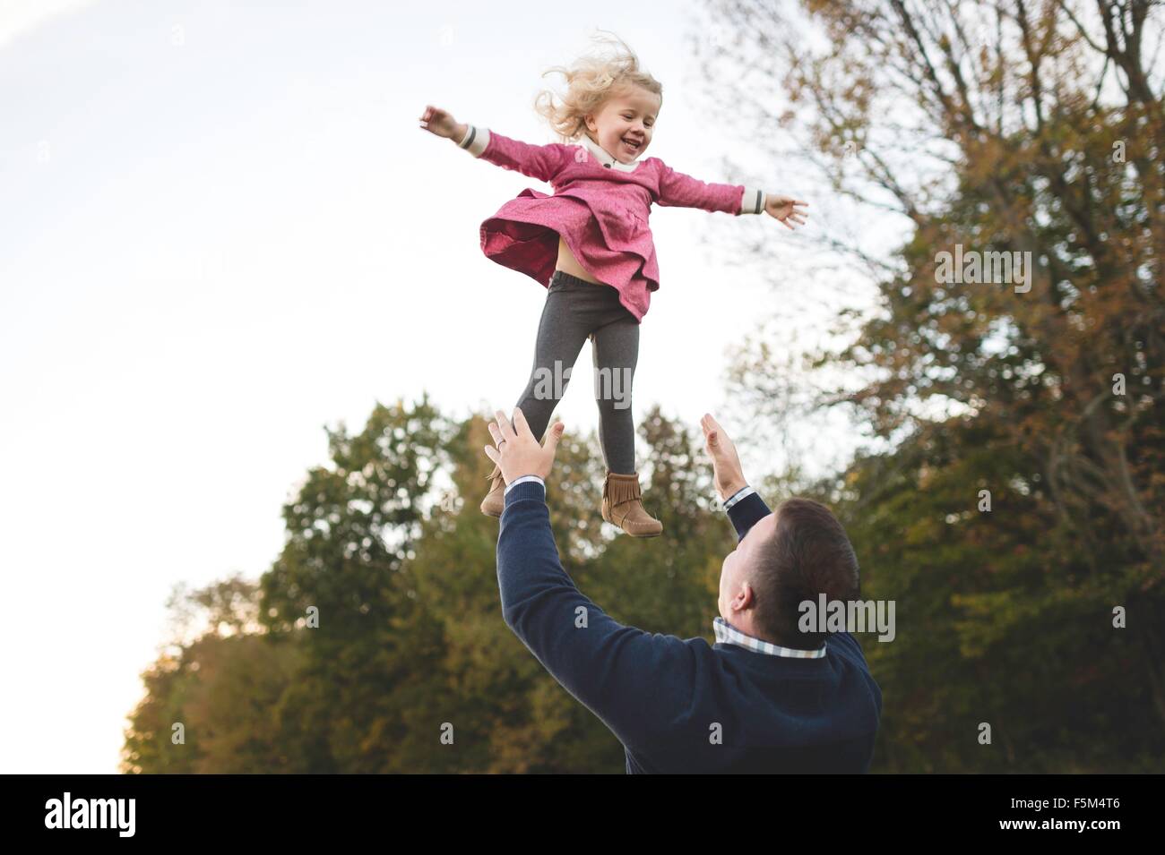 Mid adult man throwing young daughter mid air Stock Photo