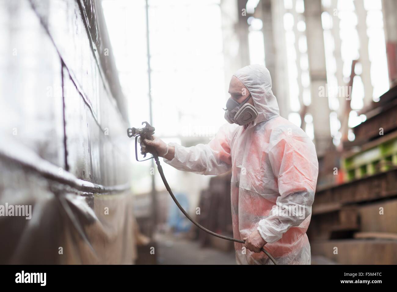 Worker spray painting boat in shipyard Stock Photo