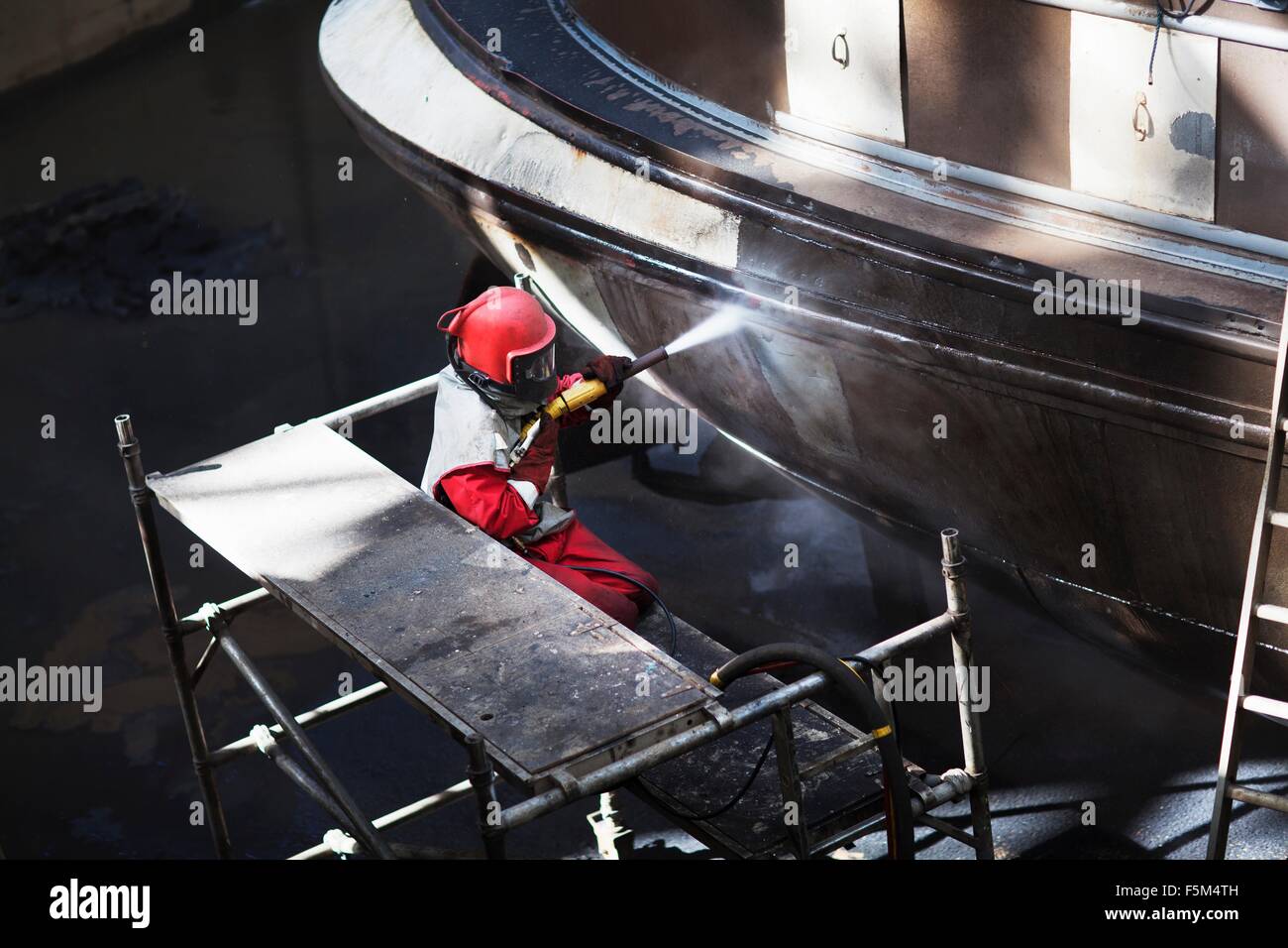 Worker cleaning hull of boat with high pressure hose in shipyard Stock Photo