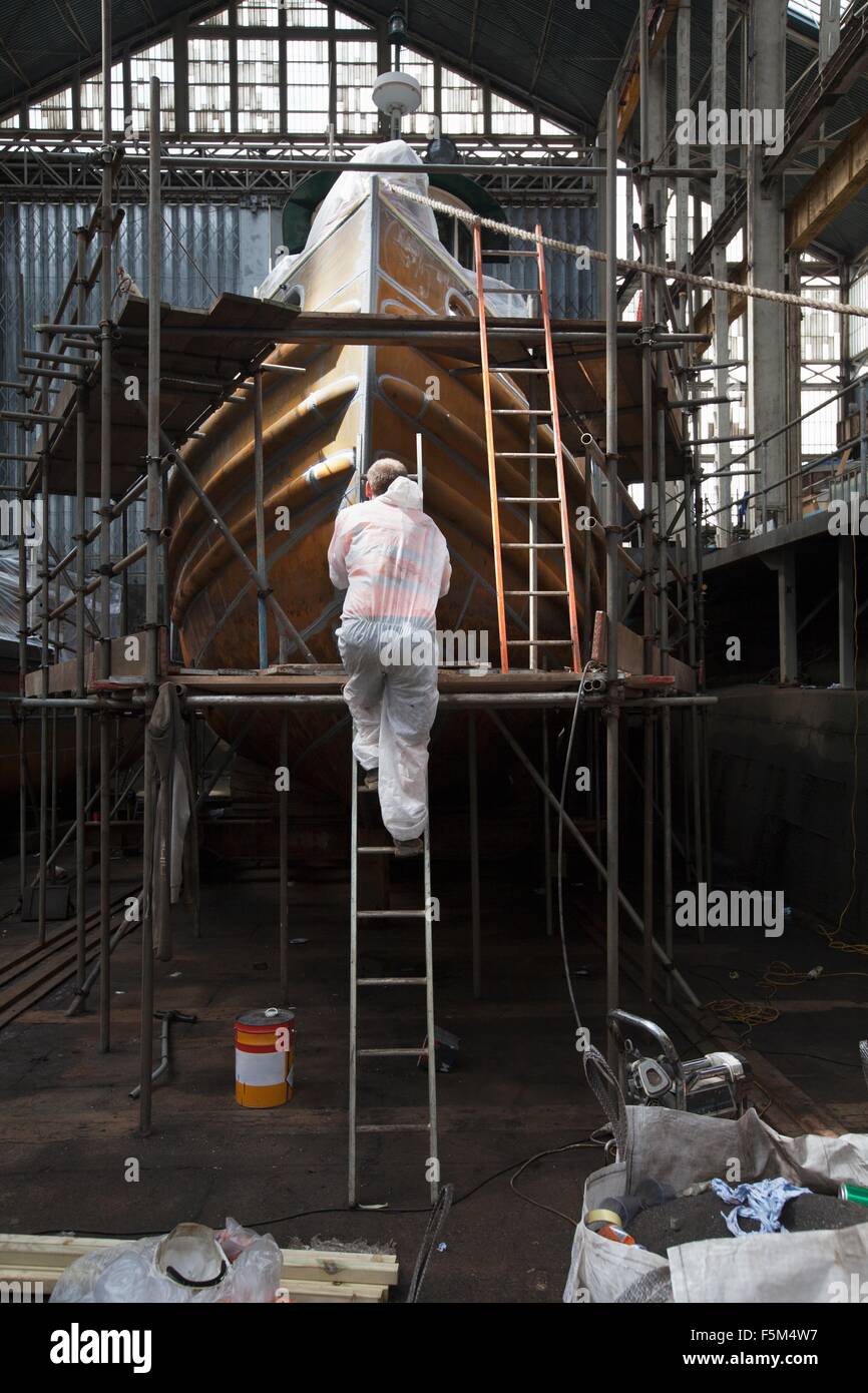 Worker climbing ladder to spray paint boat in shipyard Stock Photo