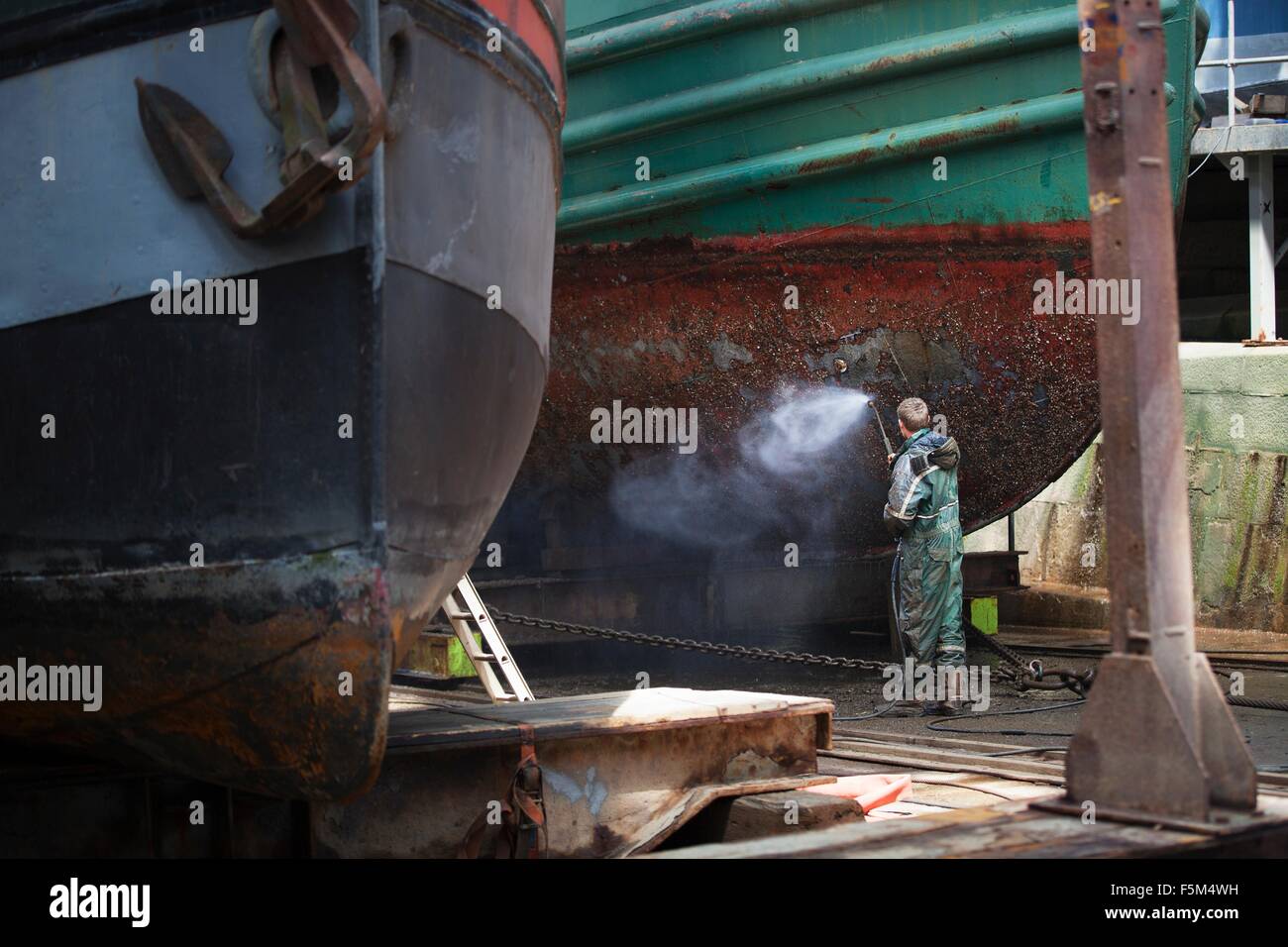 Shipyard worker cleaning boat hull with high pressure hose Stock Photo
