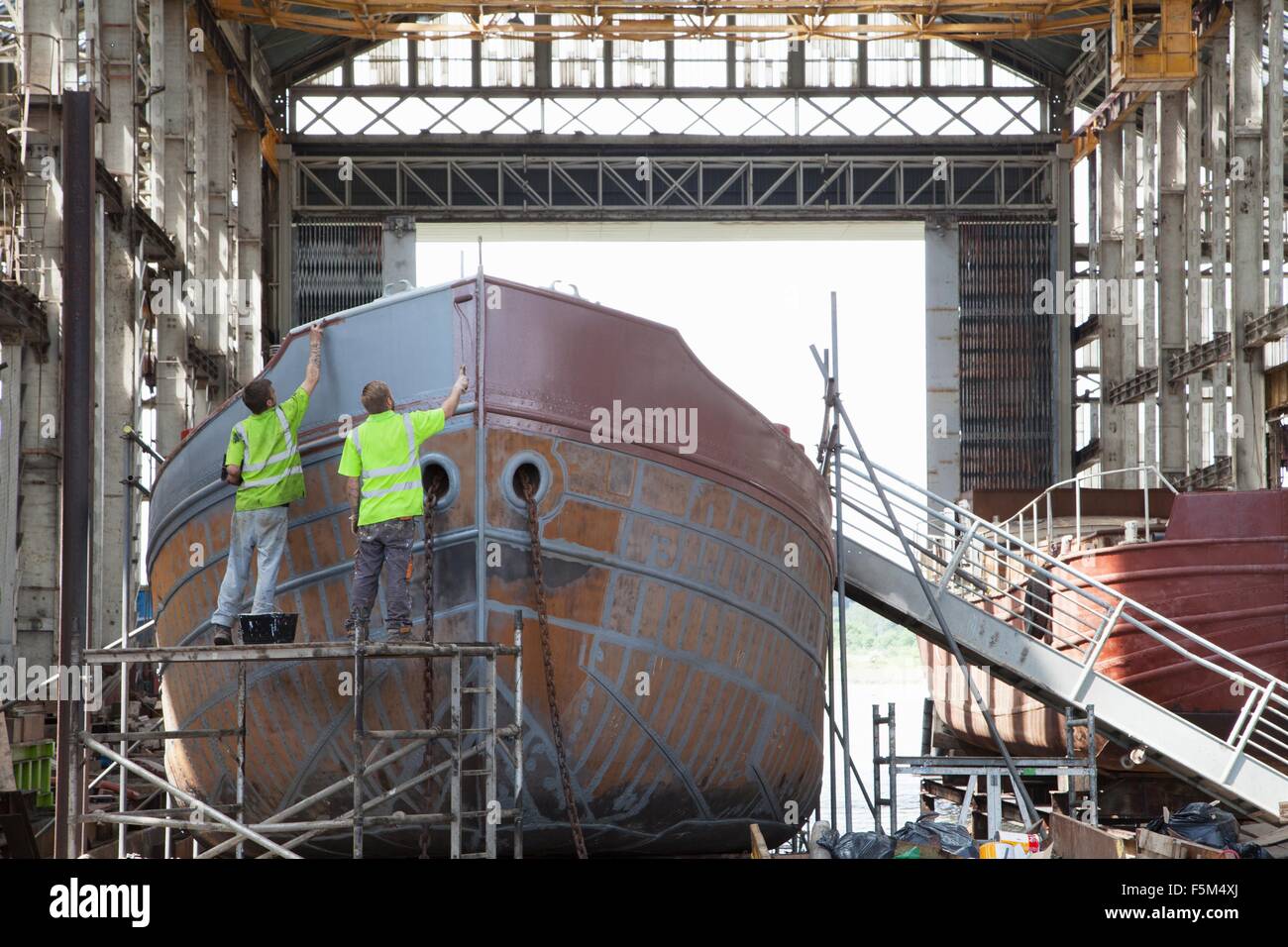 Two workers painting boat in shipyard Stock Photo