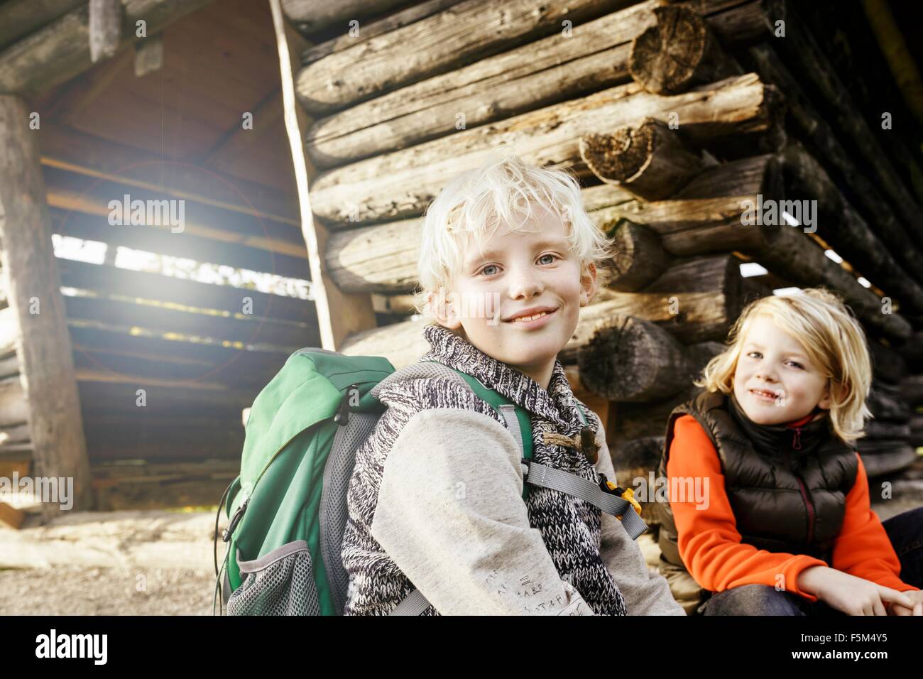 Blonde haired brother and sister sitting outside log cabin looking at camera smiling Stock Photo