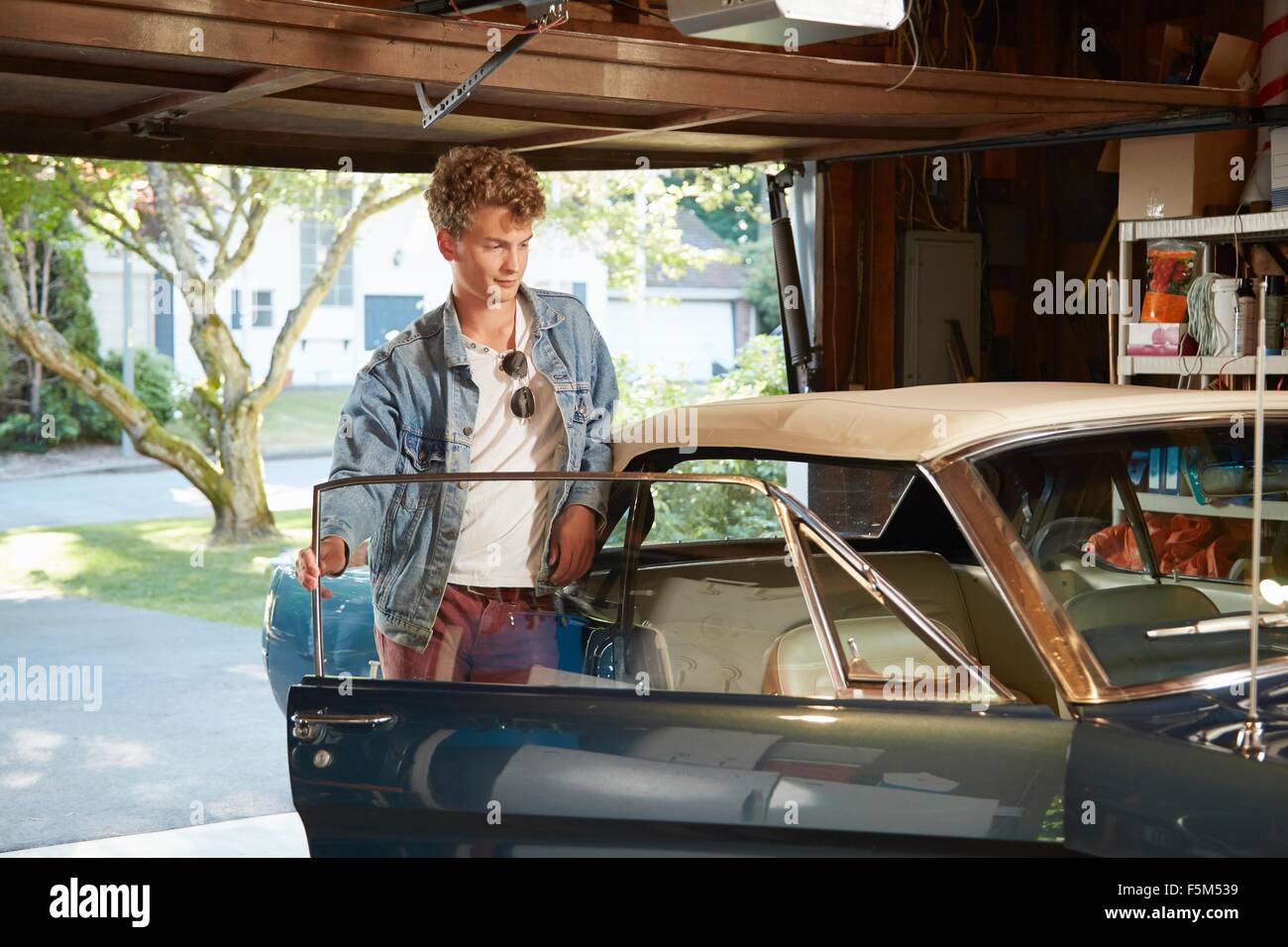 Young man in garage opening door of vintage car Stock Photo