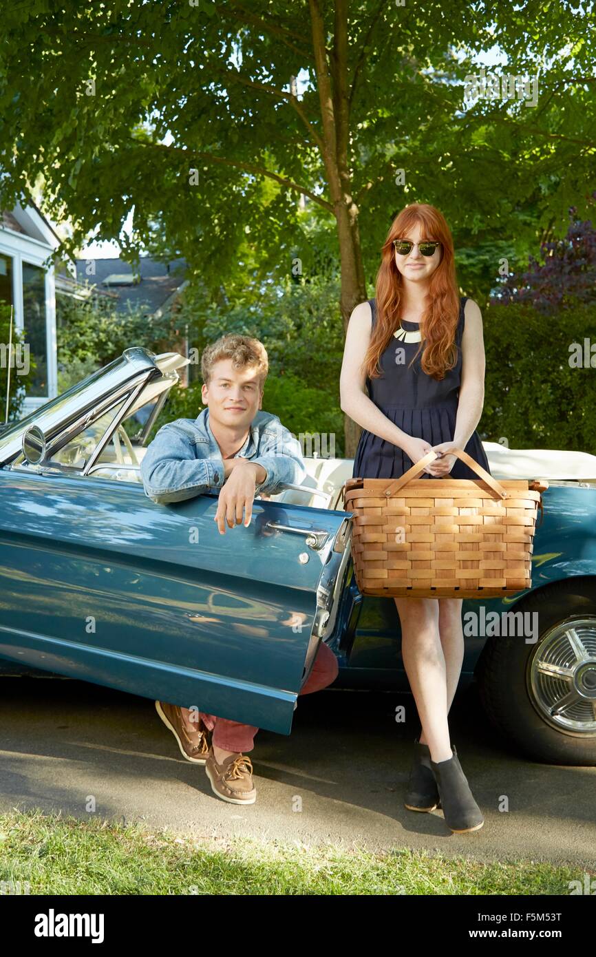 Portrait of young couple with vintage convertible holding picnic basket Stock Photo