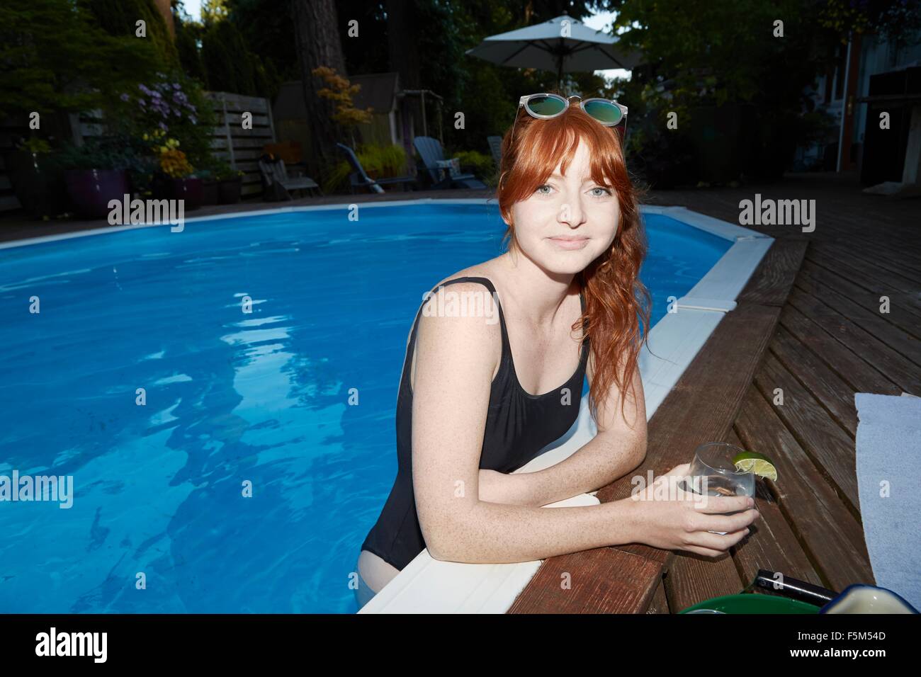 Portrait of young woman with long red hair in swimming pool at dusk Stock Photo