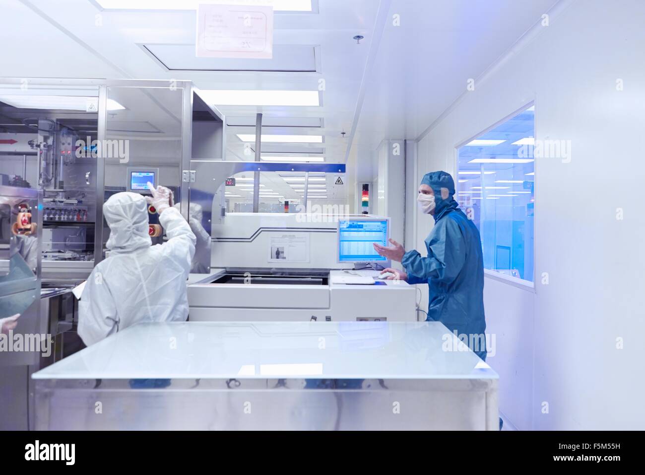 Workers using manufacturing machinery in flexible electronics factory clean room Stock Photo
