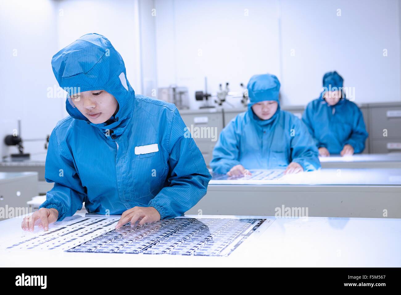 Female workers inspecting flex circuits in flexible electronics factory clean room Stock Photo