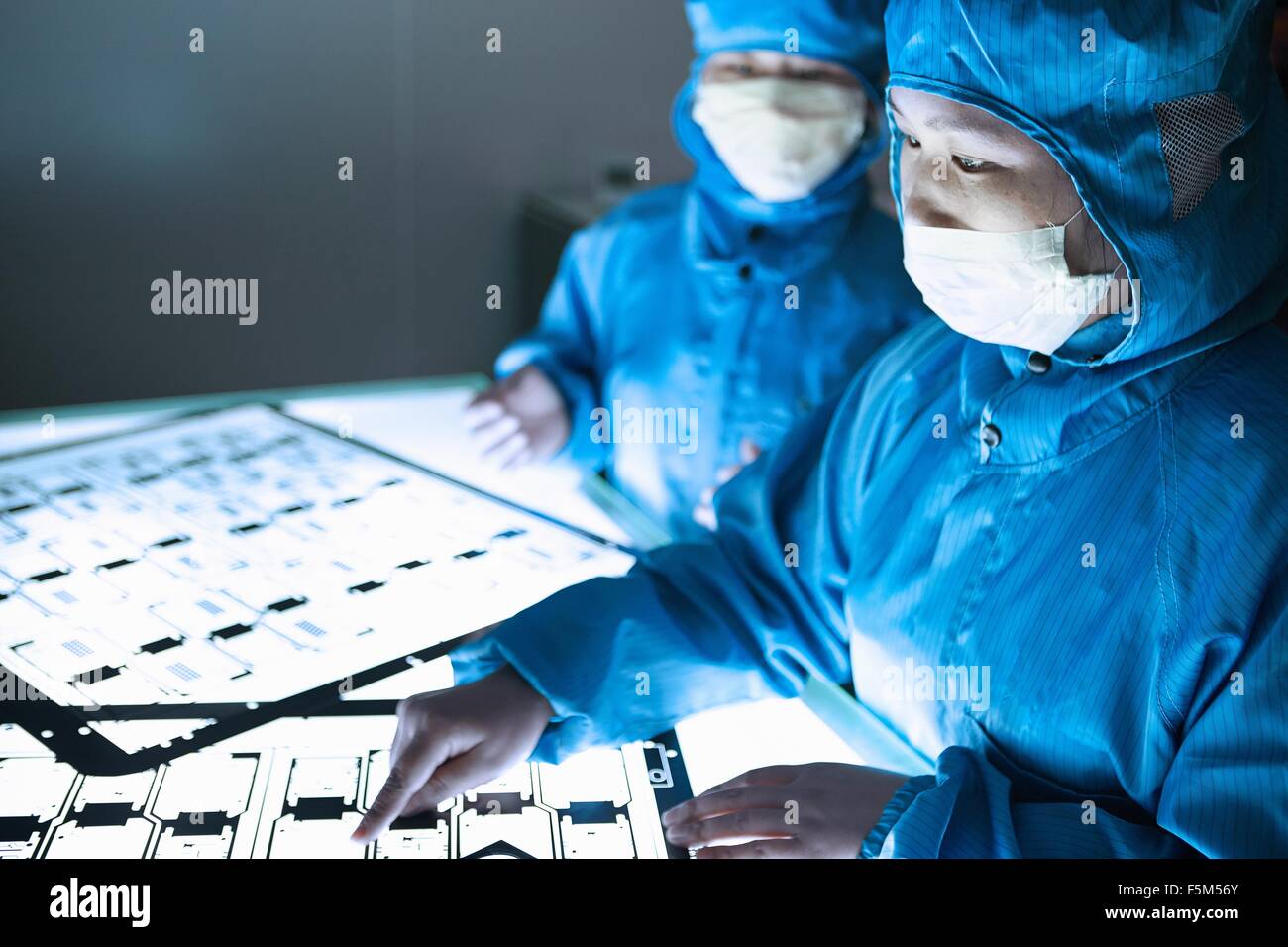 Female workers pointing at flex circuit on lightbox in flexible electronics factory clean room Stock Photo