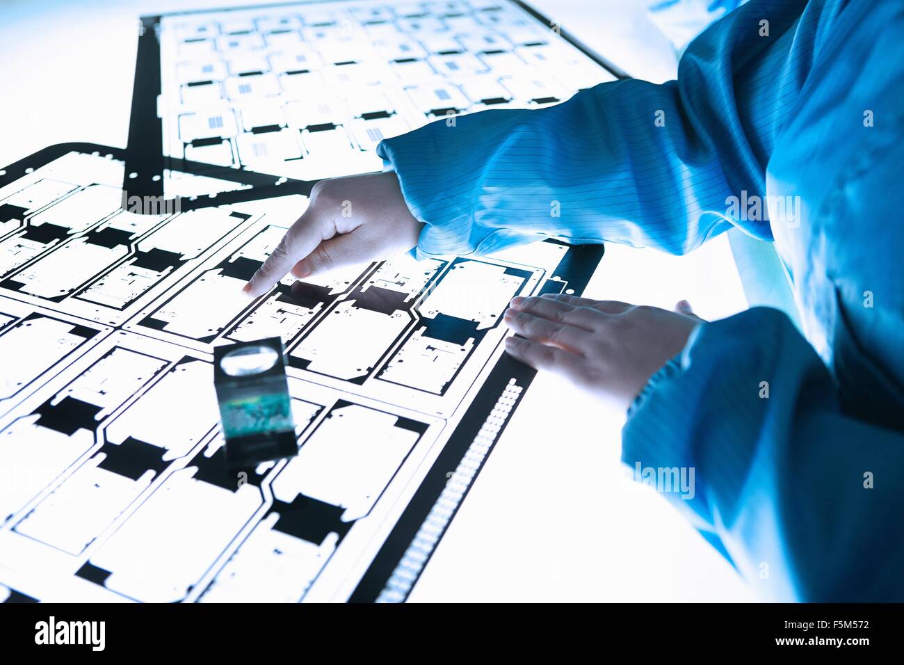 Hands of female worker inspecting flex circuit on lightbox in flexible electronics factory clean room Stock Photo