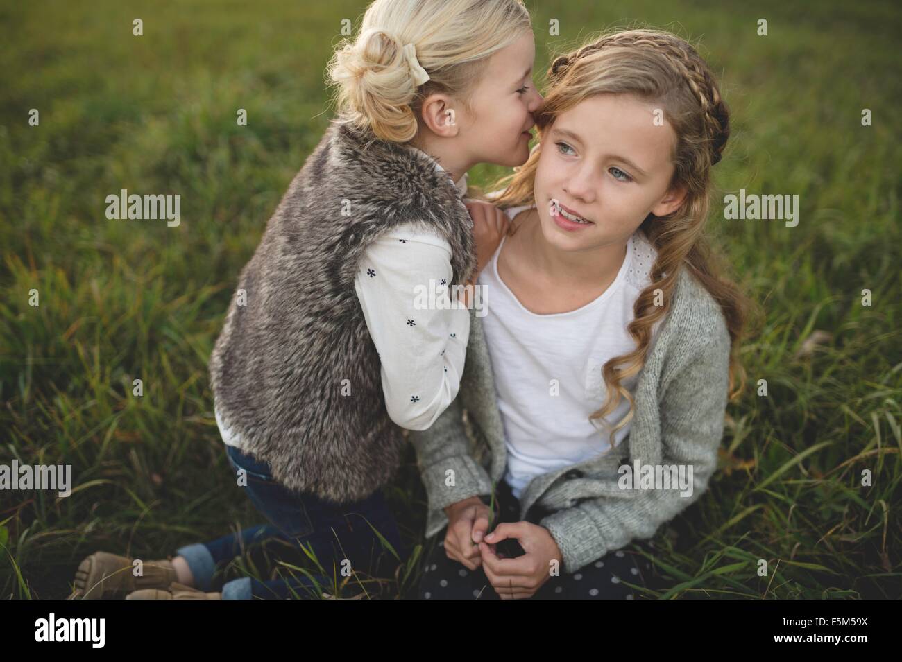 Young girl whispering in sister's ear, outdoors Stock Photo