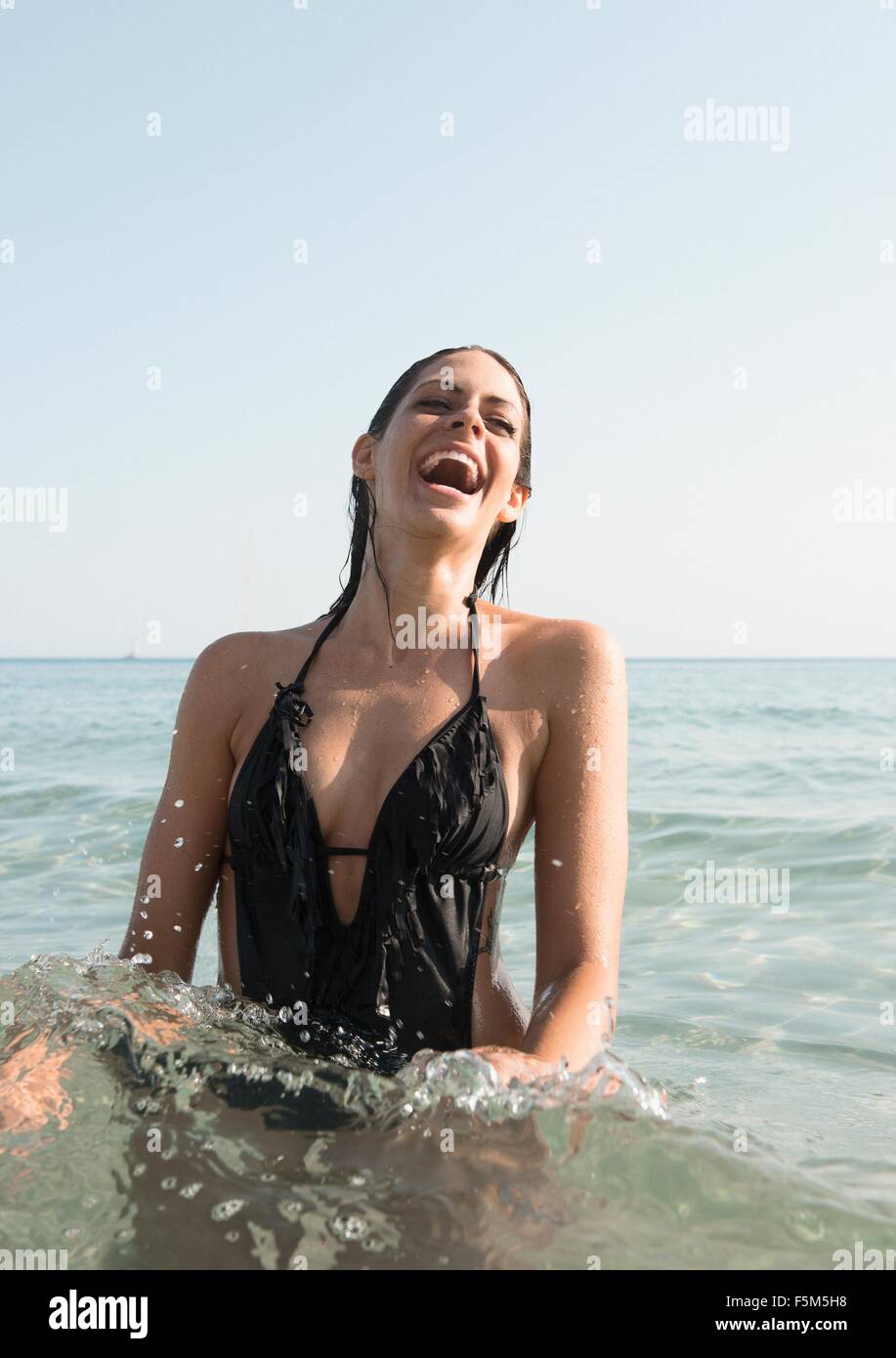 Portrait of young woman wearing bathing costume splashing in sea Stock Photo