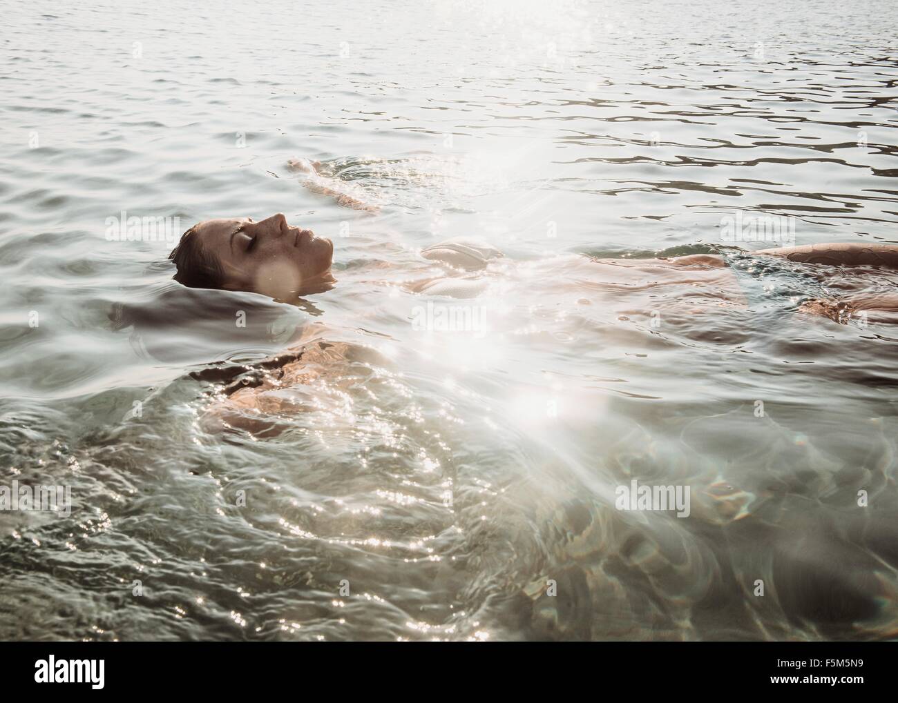 Beautiful young woman floating in sunlit sea Stock Photo