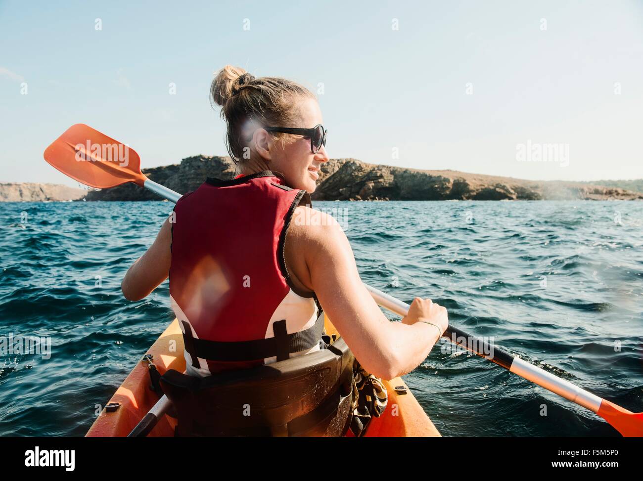Rear view of mid adult woman sea kayaking, Menorca, Balearic islands, Spain Stock Photo