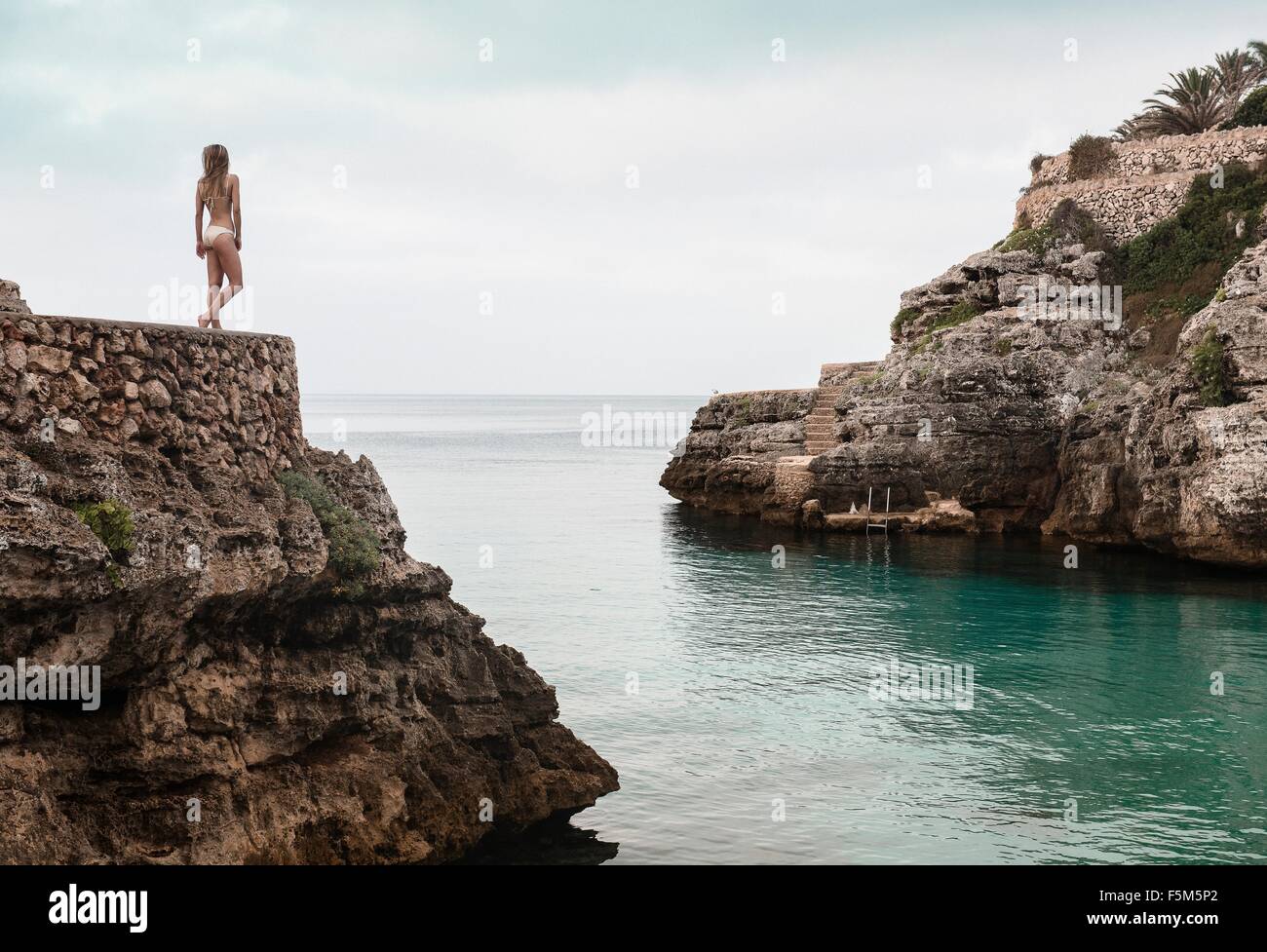 Rear view of young woman in bikini looking out from Cala en Brut, Menorca, Balearic islands, Spain Stock Photo