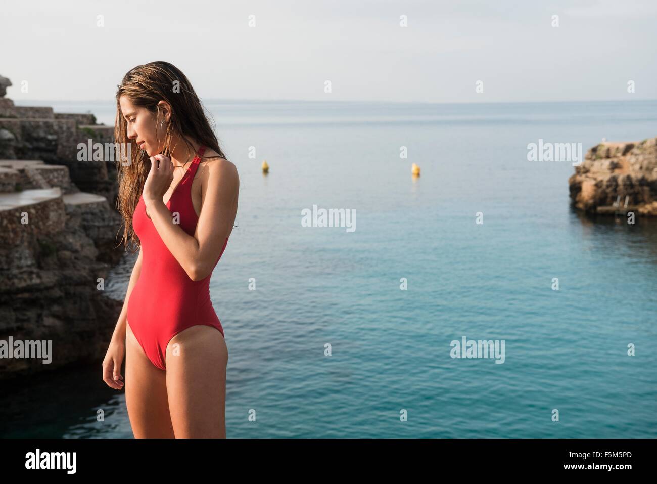 Young woman in swimming costume looking down at Cala en Brut, Menorca, Balearic islands, Spain Stock Photo