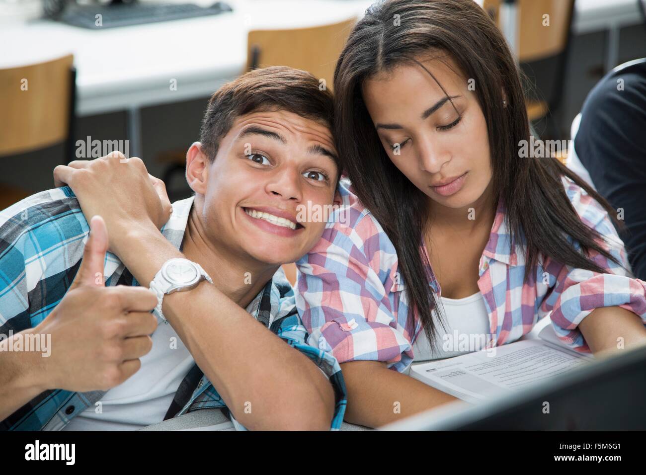 Portrait of teenage boy with cheesy grin and girl with eyes closed in class Stock Photo