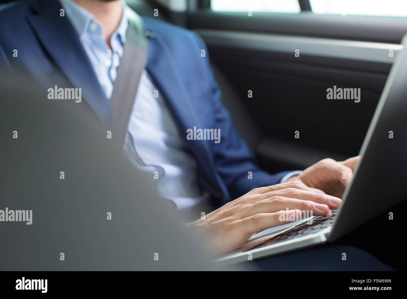 Young businessman chatting typing on laptop in back seat of car Stock Photo