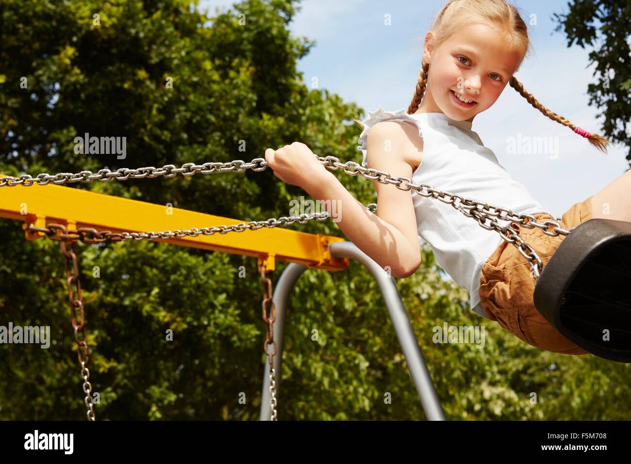 Girl with pigtails on swing looking at camera smiling Stock Photo