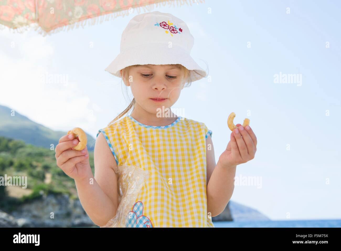 Girl wearing sunhat eating doughnut on beach Stock Photo