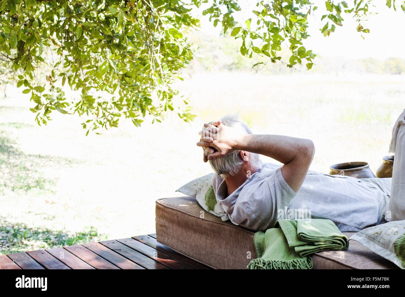 Senior man relaxing on daybed at safari lodge, Kafue National Park, Zambia Stock Photo