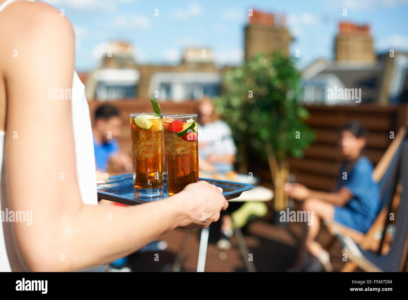 Woman carrying tray of cocktails at rooftop party Stock Photo
