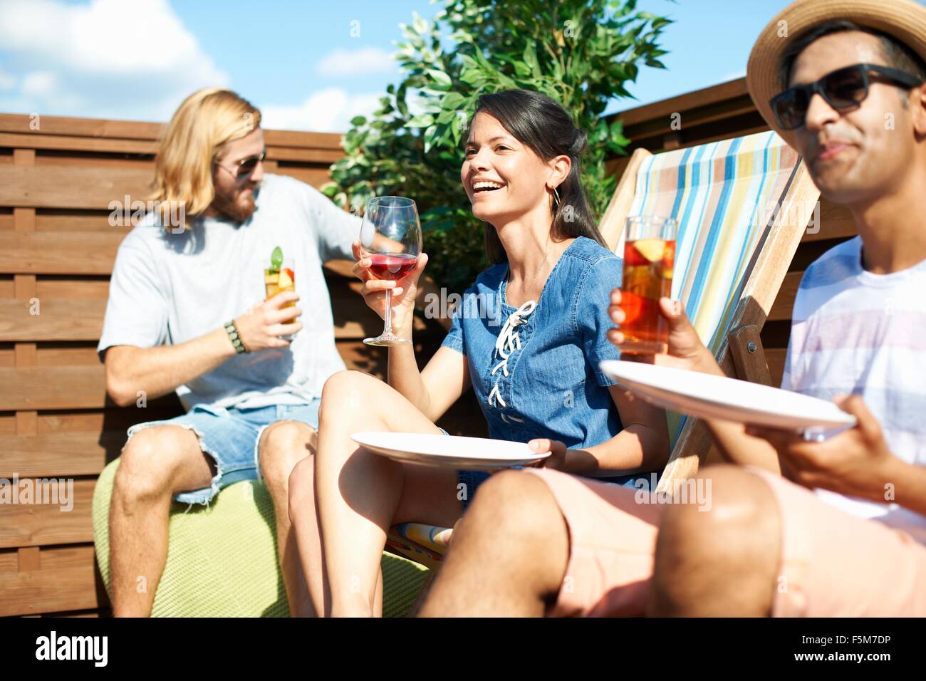Adult friends sitting on deck chairs drinking at rooftop party Stock Photo
