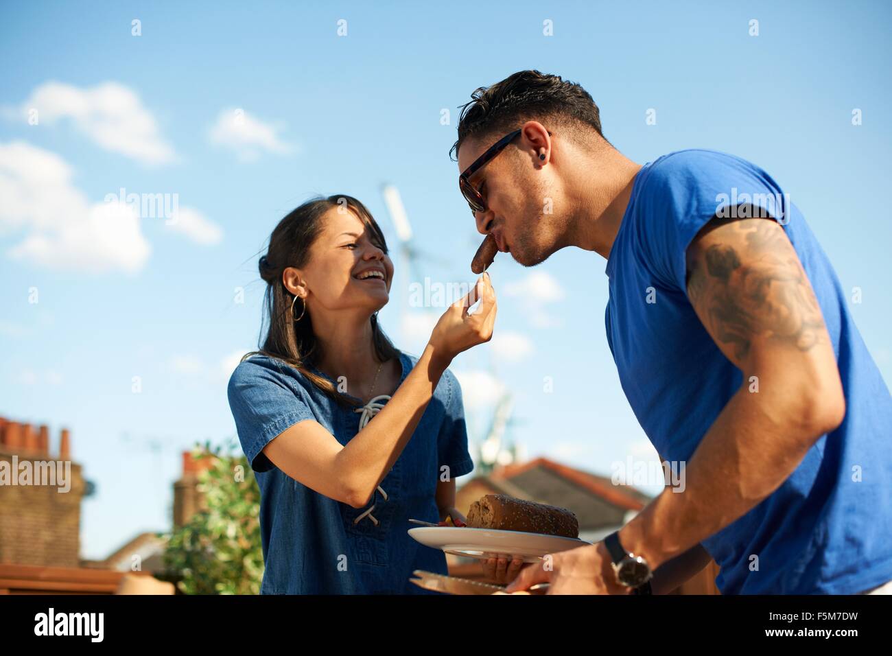 Mid adult woman feeding sausage to boyfriend at rooftop party Stock Photo
