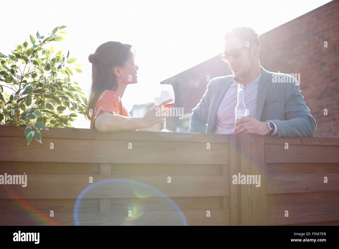 Mid adult couple chatting at fence at rooftop party Stock Photo