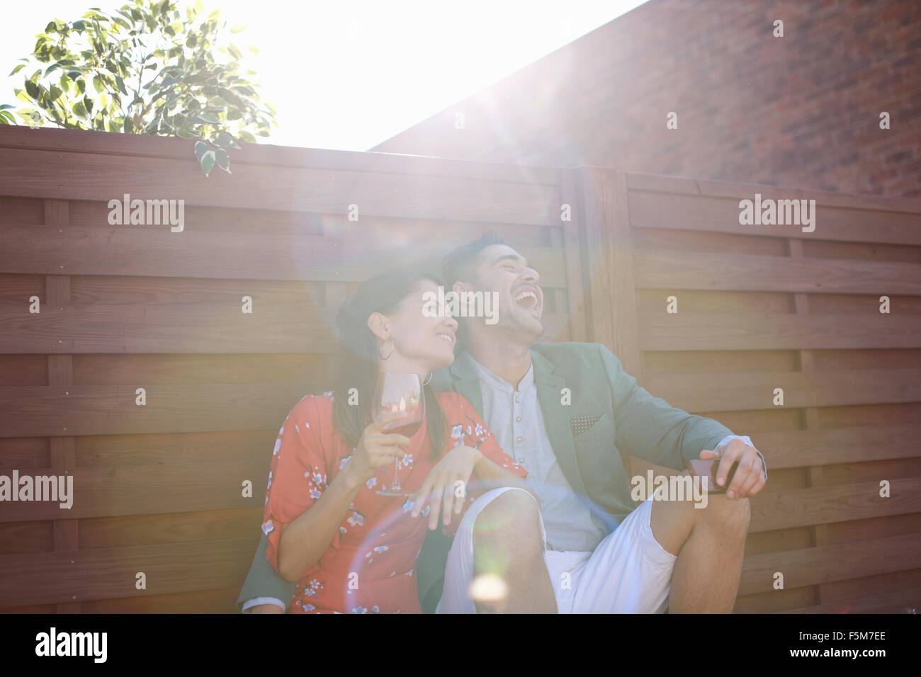 Relaxed mid adult couple laughing and drinking at rooftop party Stock Photo