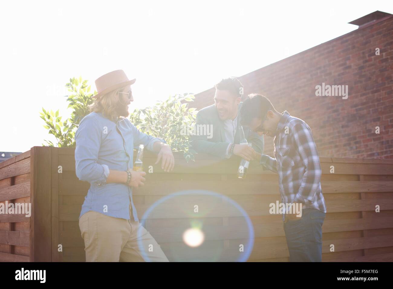 Three male friends chatting and drinking beer at rooftop party Stock Photo