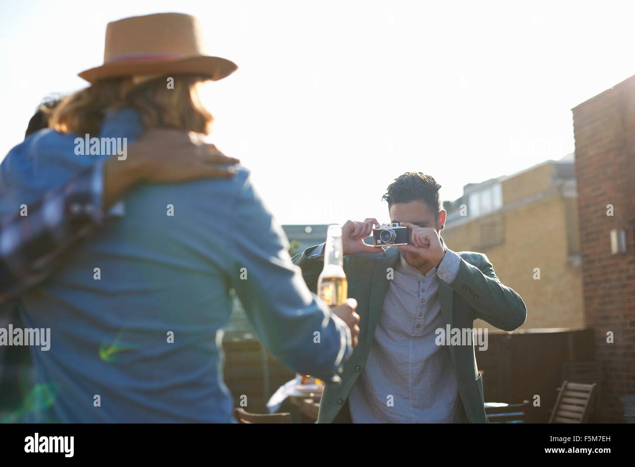 Young man photographing male friends at rooftop party Stock Photo