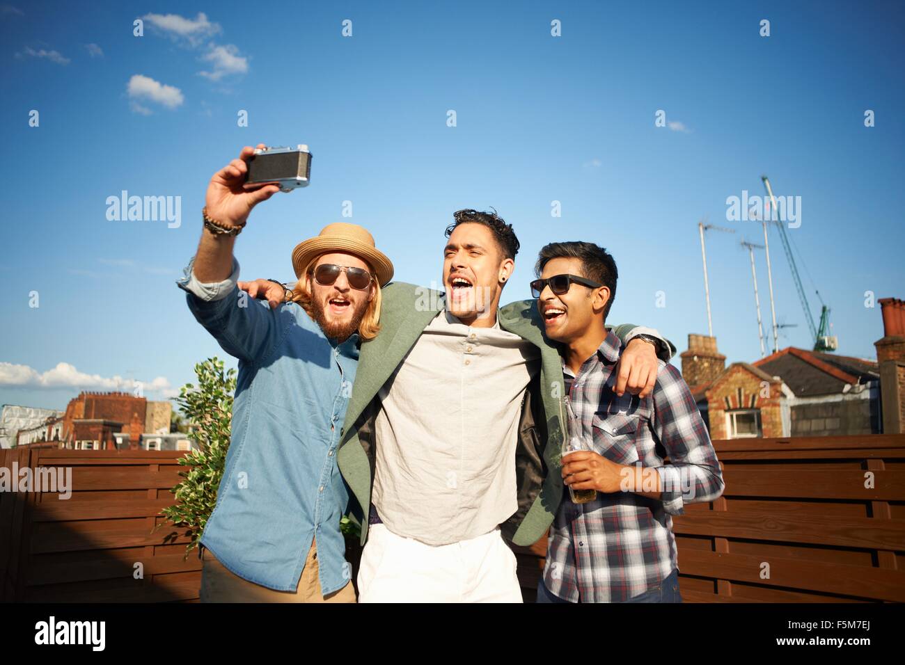Three male friends taking camera selfie at rooftop party Stock Photo