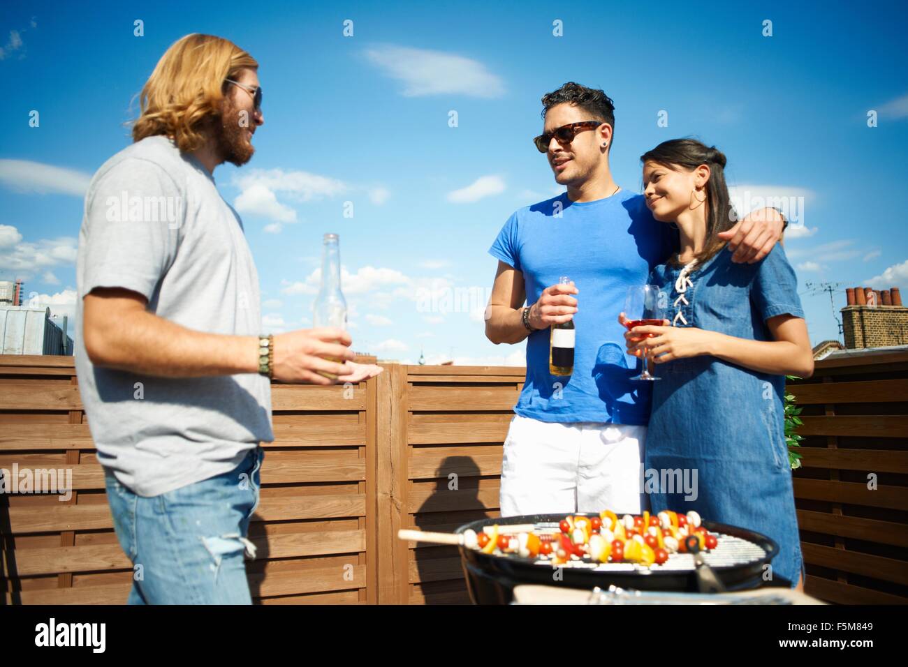 Couple chatting to male friend at rooftop party Stock Photo