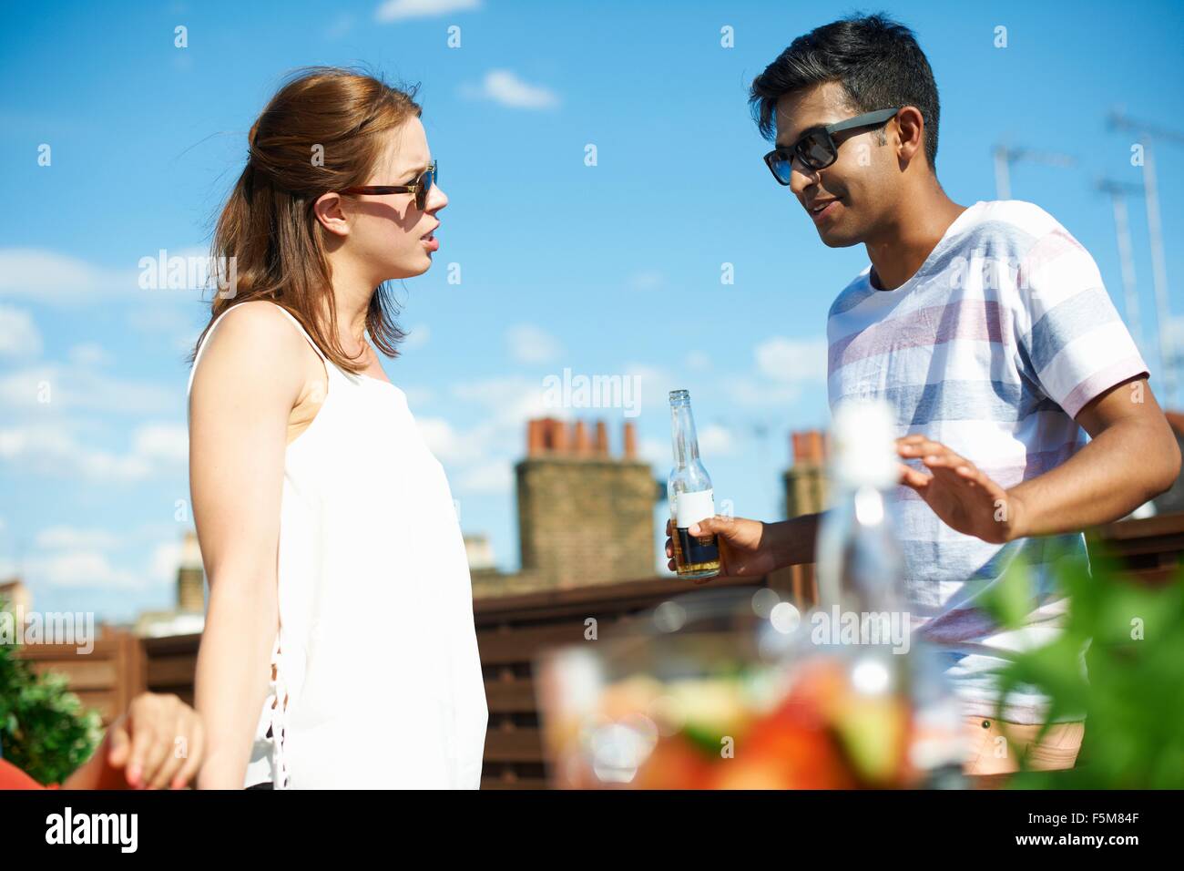 Couple chatting and drinking beer at rooftop party Stock Photo