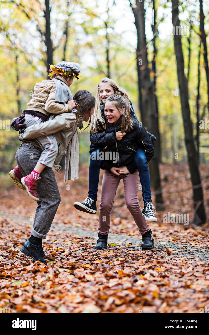 Mother and daughters playing piggyback ride in autumn forest Stock Photo