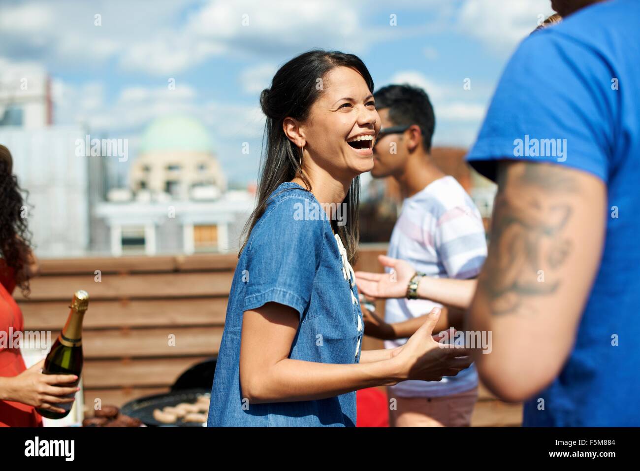 Female and male friends laughing and chatting at rooftop barbecue Stock Photo