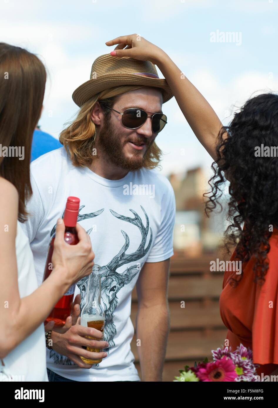 Woman putting straw hat on male friend at rooftop party Stock Photo